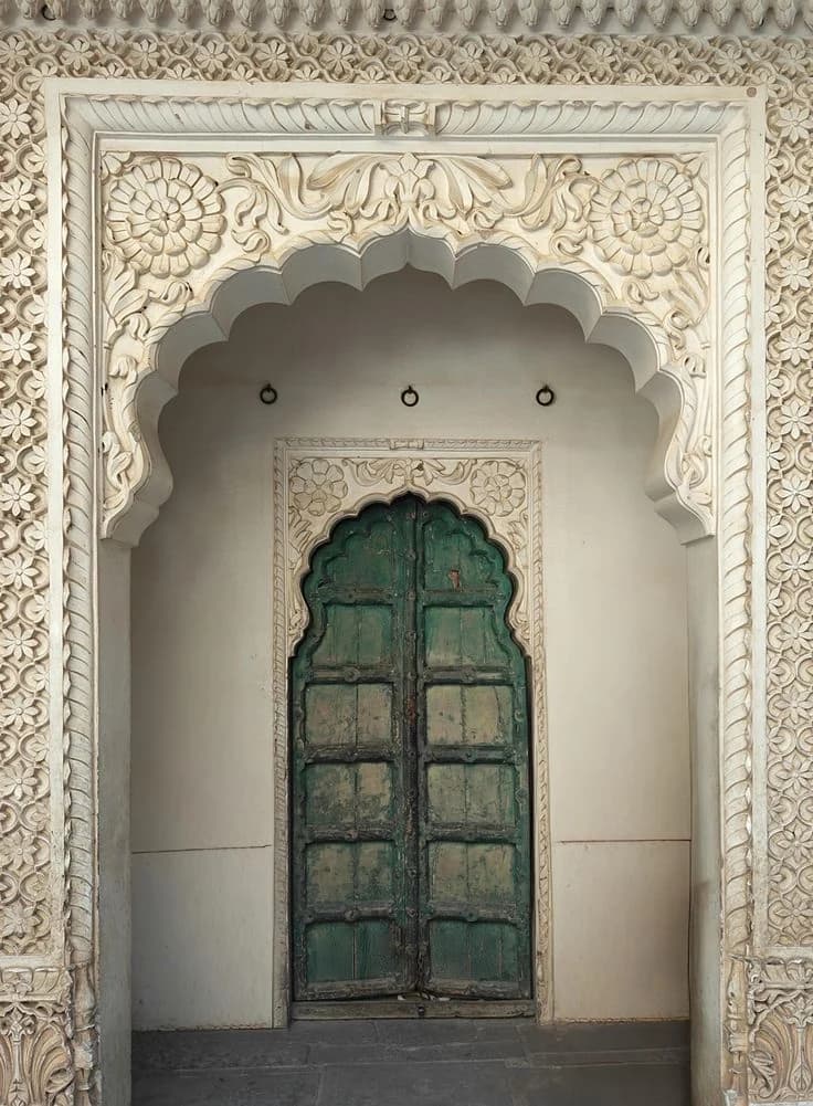 A carved white marble doorway with a weathered green door