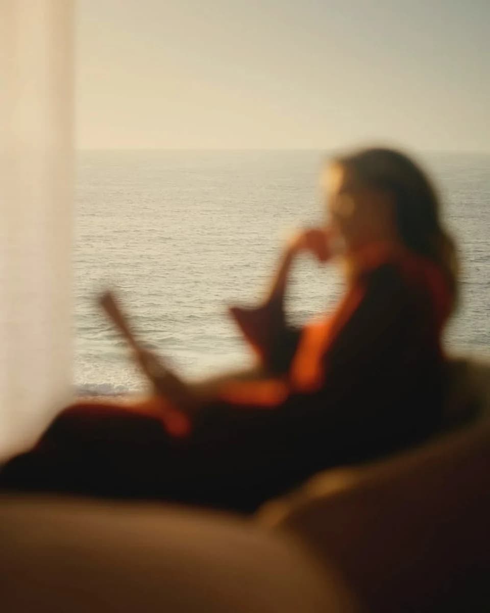 A woman reading by a window above the sea